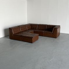 a brown leather couch sitting on top of a cement floor next to a white wall