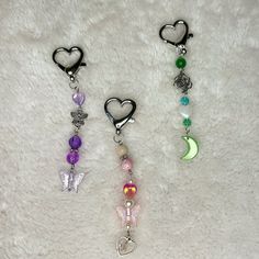 three different colored beads with hearts and butterflies hanging from them on a white surface next to each other