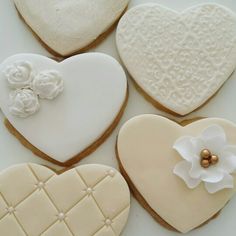 four heart shaped cookies decorated with white icing and flower decorations on top of each cookie