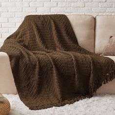 a brown blanket sitting on top of a white couch next to a pillow and chair