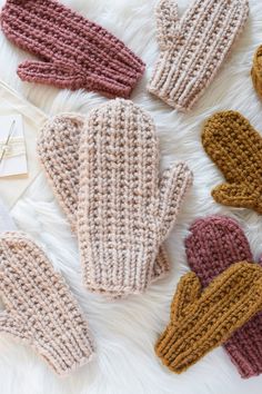 knitted mittens laid out on top of a white furnishing with tags attached to them