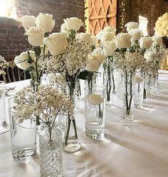 white roses and baby's breath in vases lined up on a long table