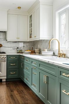 a kitchen with green cabinets and marble counter tops, gold pulls on the faucet