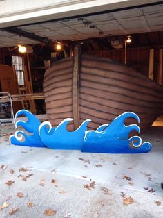 a large wooden boat sitting on top of a garage floor next to a pile of leaves