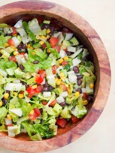 a wooden bowl filled with lettuce, black beans, corn and tomato salad