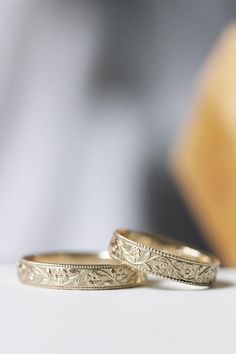 two wedding rings sitting next to each other on top of a white tablecloth with a yellow chair in the background