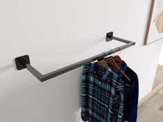 a coat rack with clothes hanging on it next to a white wall and some pictures