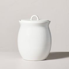 a white ceramic container with a handle on the top is sitting in front of a wall