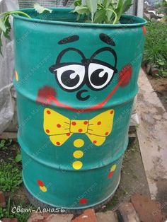 a large green barrel with a face painted on it and plants growing out of it