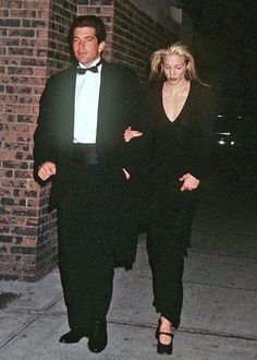 the man and woman are walking down the sidewalk in tuxedo suits, one is wearing a black dress