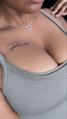 a woman with a tattoo on her chest wearing a gray top and silver bracelets