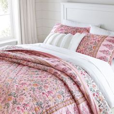 a bed with pink and white comforters in a bedroom next to a window,