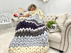 a woman is laying on a couch with a blanket over her head and holding a cup