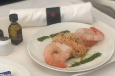 a white plate topped with shrimp and pasta on top of a table next to bottles of olive oil