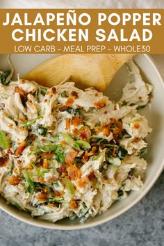 a white bowl filled with chicken salad next to a wooden spoon on top of a table