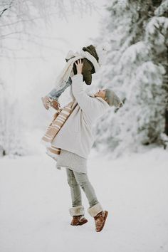 a woman walking in the snow carrying a child on her back and talking on a cell phone