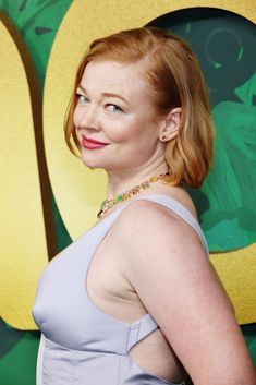 a woman with red hair wearing a blue dress and smiling at the camera while standing in front of a green wall