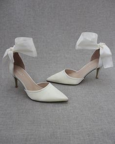 a pair of white high heel shoes with bows on the toe and heels are shown