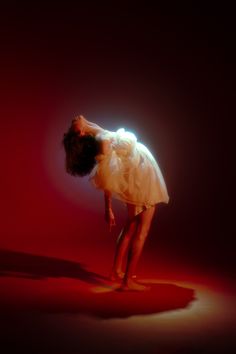 a woman in a white dress is bending over with her head on the floor and hands behind her back