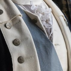 a close up of a man wearing a white jacket and blue vest with buttons on it