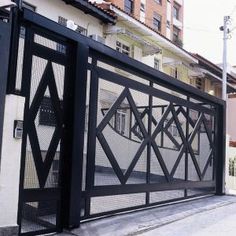 an iron gate with geometric designs on the side of a building next to a street