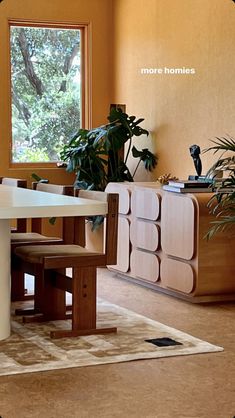 a dining room table and chairs in front of a window with potted plants on it