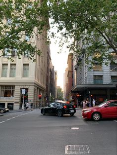 two cars are driving down the street in front of tall buildings with trees on both sides