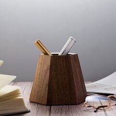 a wooden pen holder sitting on top of a table next to glasses and books,