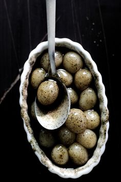 a white bowl filled with brown speckled eggs on top of a wooden table next to a spoon