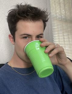 a young man drinking from a green cup