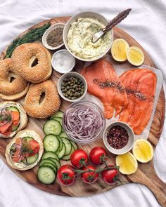 a wooden platter topped with bagels, salmon, cucumbers and other foods