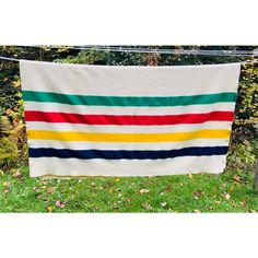 a multicolored striped blanket hanging on a clothes line in the grass next to some trees