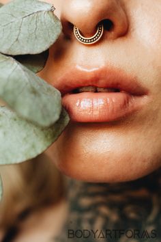 a woman with piercings on her nose is holding a leaf to her face and looking at the camera