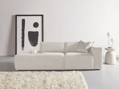 a living room with a white couch, rug and black framed painting on the wall