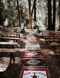 an outdoor area with benches and rugs on the ground in front of some trees