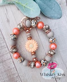 a bracelet with charms and flowers on it sitting on a wooden table next to leaves