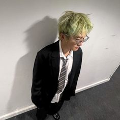 a man with green hair wearing glasses and a suit standing in front of a wall