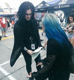 two women with blue hair are talking to each other at an outdoor event in the street