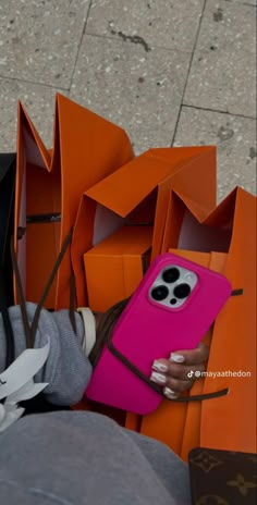 a woman is holding an orange and pink cellphone in her hand while sitting on the ground