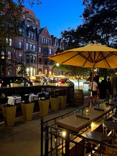 an outdoor dining area with tables and umbrellas lit up at night in the city