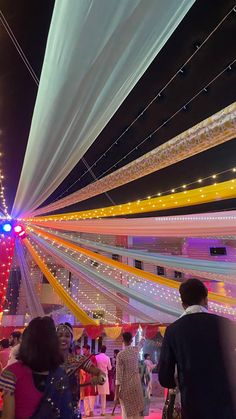 people are walking around in an open area with lights on the ceiling and colorful streamers