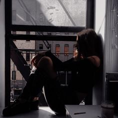 a woman is sitting on a window sill looking out the window at the city