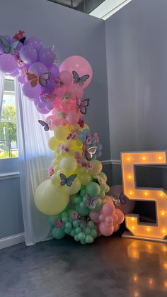 10 foot color blocked balloon garland with silk flowers and paper butterflies next to a marquee number 5 Butterfly And Flower Balloon Arch, Balloon Garland With Flowers And Butterflies, Flowers And Butterflies Decorations, Fairy Theme Balloon Decoration, Pastel Butterfly Balloon Garland, Butterfly And Rainbow Birthday Party, Unicorns And Butterflies Party, Butterfly And Flower Birthday Party, Flower And Butterfly Birthday Theme