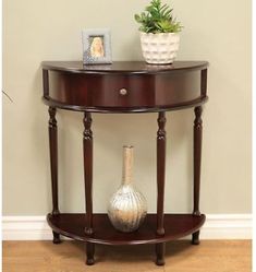 a round wooden table with a vase on top and a small plant in the corner