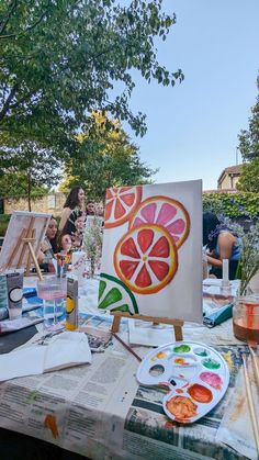 people are painting on canvases at an outdoor table with watermelon and oranges