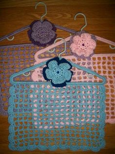 three crocheted purses hanging from hooks on a wooden floor with clothes pins attached to them