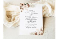 a wedding card with flowers on it next to a white napkin and a flower bouquet