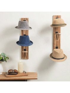 three hats are hanging on the wall next to a candle and some other items in a vase