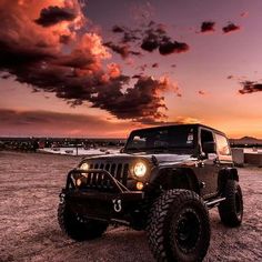 a jeep is parked in the middle of a dirt field at sunset with clouds above it