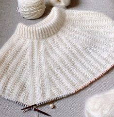 a white knitted cape sitting on top of a table next to yarn and scissors